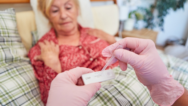 Medicinski radnik u rukavicama radi CRP test kod starije žene koja leži u krevetu