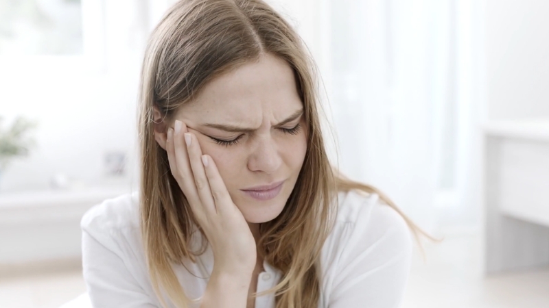 Mlada žena drži obraz i ima bolnu grimasu zbog jake zubobolje