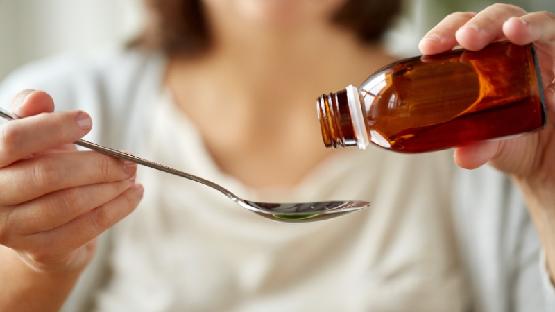 Osoba sipa sirup za kašalj iz bočice u kašiku