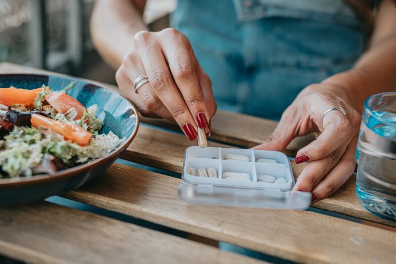 prikaz osobe koja uzima suplemente iz kutije, pored nje salata