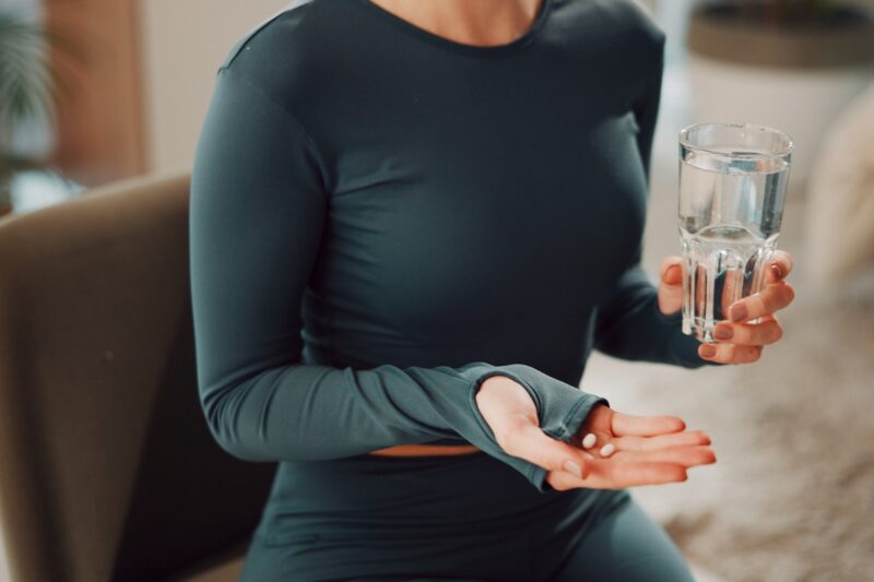 prikaz osobe koja drži čašu vode i suplemente u drugoj ruci