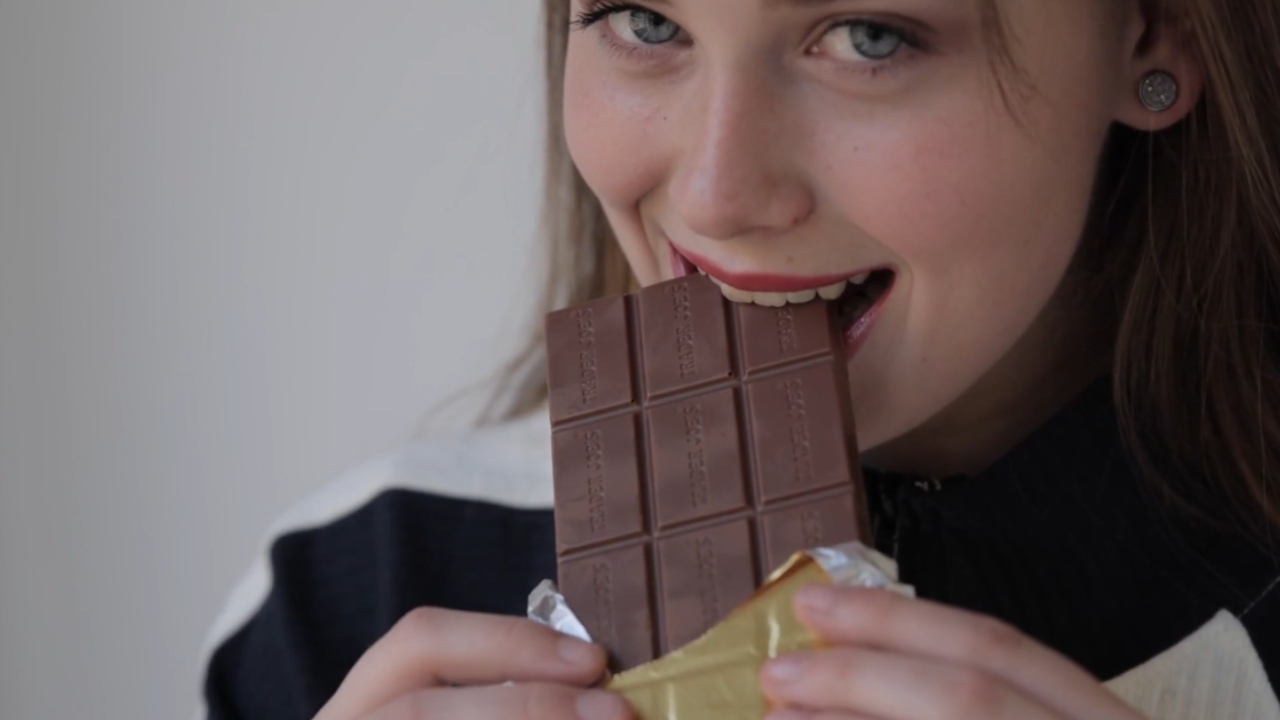 Žena grize tablu mlečne čokolade i drži je u rukama.